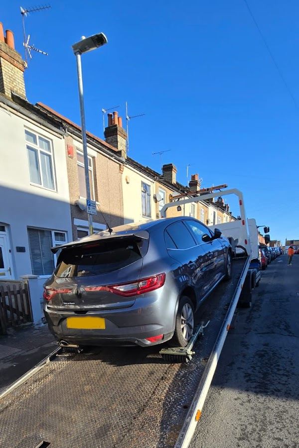 Prompt Recovery DAF LF flatbed truck loading a grey Renault Megane hatchback on a residential street in bright sunshine