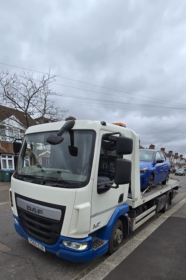 Prompt Recovery DAF LF flatbed truck with a blue hatchback car loaded, collected from a residential street on an overcast day