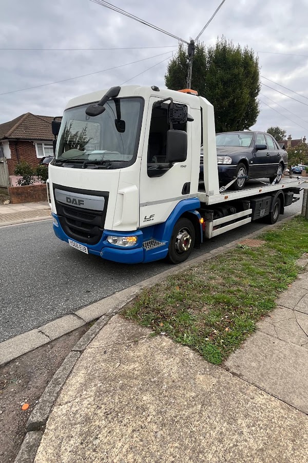 Prompt Recovery DAF LF flatbed truck with a dark SUV loaded, parked on a residential corner on a cloudy autumn day