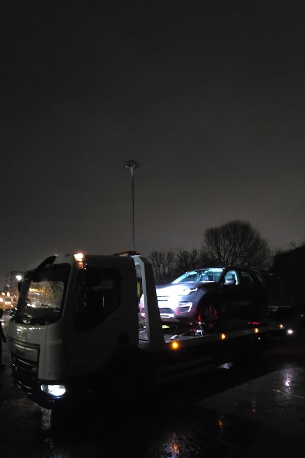 Prompt Recovery flatbed truck at night in wet conditions with a Land Rover Discovery Sport loaded on the bed
