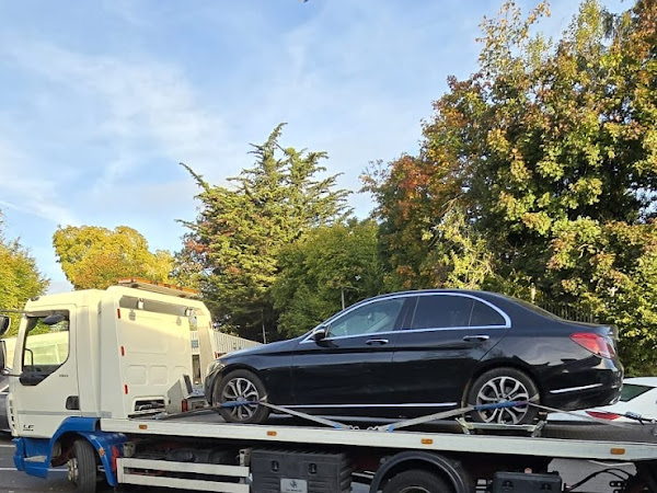 Prompt Recovery DAF LF flatbed truck transporting a black Mercedes C-Class saloon in a car park surrounded by autumn trees