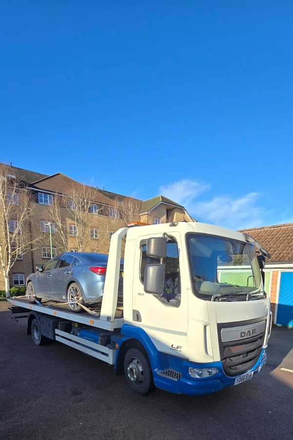 Prompt Recovery DAF LF flatbed truck with a silver saloon car loaded on the bed, parked in a residential car park on a clear day