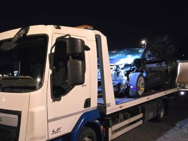 Prompt Recovery DAF LF flatbed truck at night transporting a accident-damaged car with a crumpled front end
