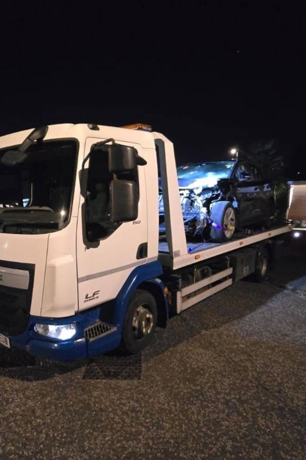 Prompt Recovery DAF LF flatbed truck at night transporting a accident-damaged car with a crumpled front end