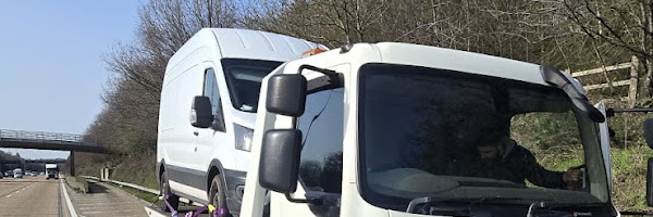 Prompt Recovery DAF LF flatbed truck on a motorway hard shoulder recovering a white panel van under a clear blue sky