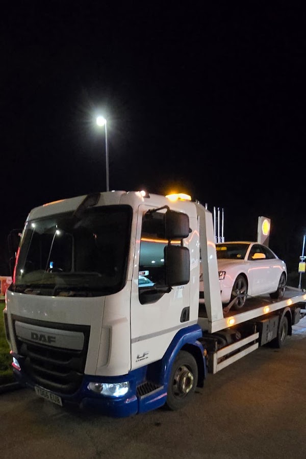Prompt Recovery DAF LF flatbed truck at night with a white saloon car loaded, parked under floodlights at a service station