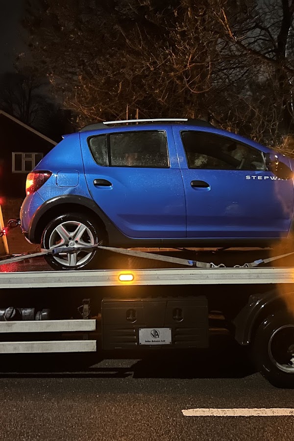 Close-up of a blue Dacia Sandero hatchback strapped securely to a Prompt Recovery DAF LF flatbed truck at night