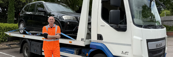 Nick standing in front of his recovery truck, with a car on the back
