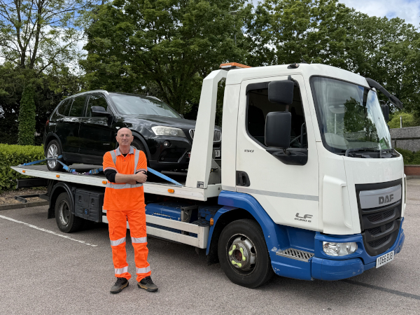 Nick standing in front of his recovery truck, with a car on the back